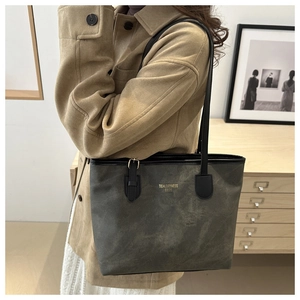 Macro detail of the dark gray tote bag featuring a gold logo and black leather strap