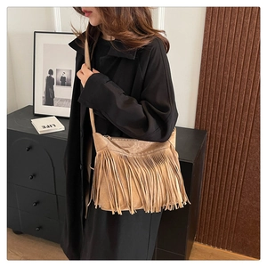 Brown suede crossbody bag with long fringes and zipper closure shown in a lifestyle setting