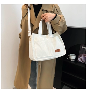 Detail of white corduroy tote bag with brown fashion patch and adjustable shoulder strap