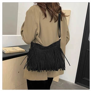 Detail of a black crossbody bag featuring long bohemian tassels and frosted matte texture