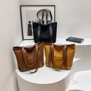 Three minimalist suede tote bags in black, brown, and yellow on a modern display stand