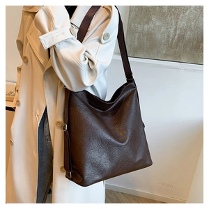 Detail of dark brown leather tote bag with adjustable silver buckle on a beige trench coat