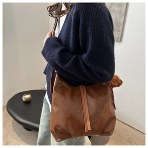 Deep brown faux leather tote bag with plush bear charm worn by a model in a casual setting