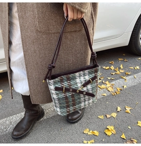Close-up of retro plaid tweed bucket bag with leather handle on street with autumn leaves
