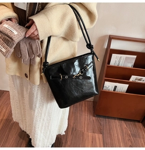 Detail of a black glossy bucket bag featuring gold metal eyelets and a buckle strap