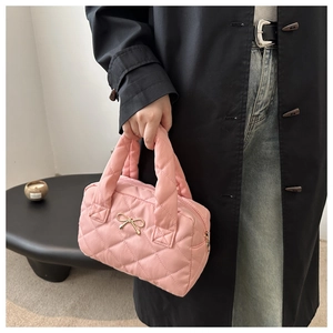 Close-up of pink quilted handbag with golden bow detail held by model in soft lighting
