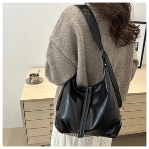 Detail of black glossy crescent shoulder bag with long leather zippers on a wide strap