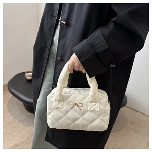 Close-up of beige quilted pillow bag featuring a gold bow metallic buckle detail