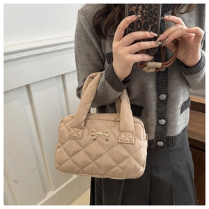 Detailed close-up of a beige quilted shoulder bag with a gold metal bow on soft fabric