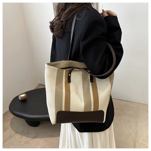 Detailed view of striped canvas tote bag with leather straps on a model's shoulder