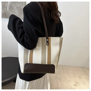 Detail of vertical striped tote bag with brown leather base and reinforced metal rivets