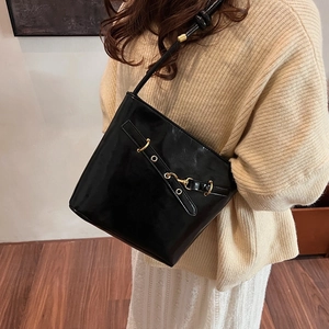 Chic black shiny bucket bag with gold hardware worn as a stylish crossbody by model