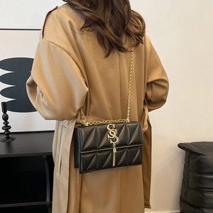 Chic black quilted crossbody bag with gold chain strap on a trench coat model