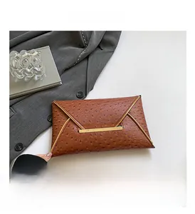 Detail of brown ostrich leather envelope clutch with gold metal bar on grey suit background