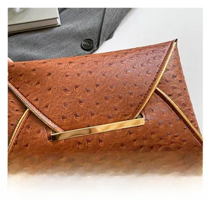 Detail of brown ostrich texture envelope clutch with a sleek gold metal accent bar