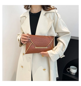 Detail of caramel brown ostrich-embossed envelope clutch with gold V-metal trim on a model