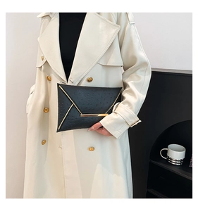 Detail of black embossed envelope clutch with gold V-shaped trim and metal clasp