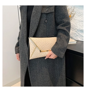 Detailed view of champagne ostrich textured envelope clutch bag with gold metallic trim