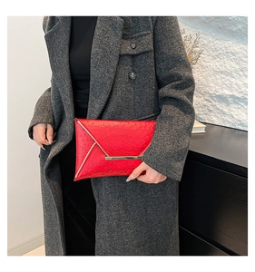 Detail view of red ostrich pattern envelope clutch with golden metal trim on grey coat