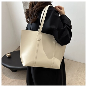 Minimalist cream tote bag styled on shoulder with black coat in a modern setting