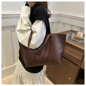 Minimalist dark brown tote bag with smooth leather finish shown on shoulder in interior setting