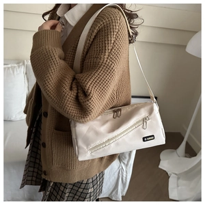 Détail du sac bandoulière en nylon crème avec double fermeture éclair et étiquette mode