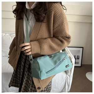 Détail d'un grand sac bandoulière en nylon vert menthe porté sur un pull en maille marron