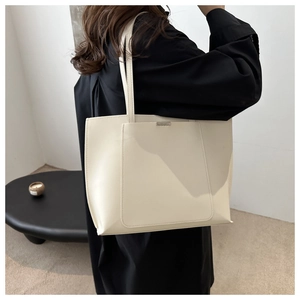 Detail of cream leather tote bag featuring a decorative metal buckle and large front pocket