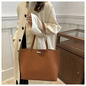 Detail of a large brown leather tote bag with silver metal bar and slim shoulder straps