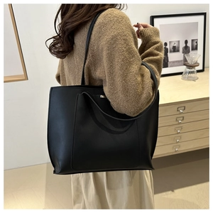 Side view of large black leather tote bag with silver metal plate on a female model
