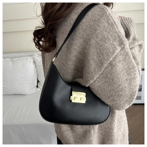 Detail of minimalist black hobo bag with a golden metal buckle on a cozy knit sweater