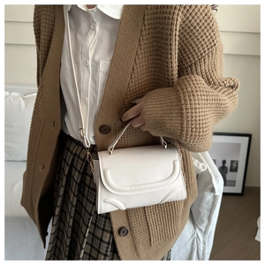 Detail der cremefarbenen Umhängetasche mit Ziernähten, kombiniert mit Retro-Strickjacke