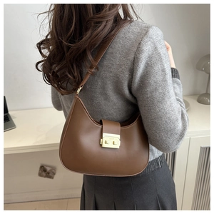 Brown leather crescent bag worn over the shoulder with a stylish minimalist outfit