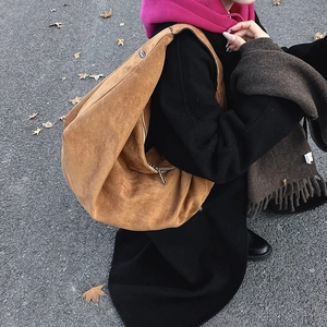 Brown suede crescent shoulder bag with metallic zipper shown in a stylish autumn outfit