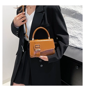 Detail of caramel brown leather handbag featuring unique asymmetric flap and square buckle