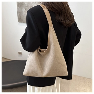 Détail d'un grand sac hobo en daim beige porté à l'épaule avec une veste de tailleur chic