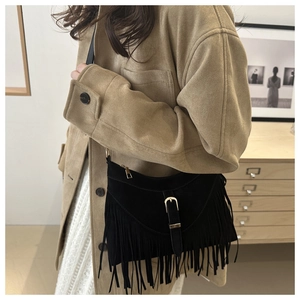 Detail of black suede shoulder bag with long bohemian tassels and metal buckle closure