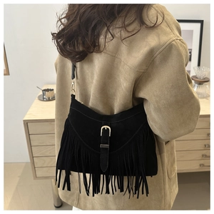Detail of black suede tote bag with long tassels and gold buckle on a model shoulder