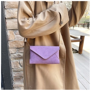 Detail of purple faux suede envelope bag with gold chain strap in outdoor setting