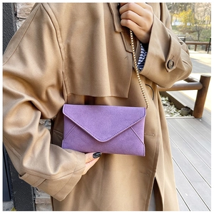 Close-up of purple matte suede envelope bag with elegant gold chain strap in sunlight