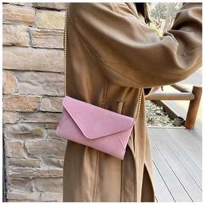 Detail of pink matte envelope crossbody bag with a gold chain strap on a camel coat