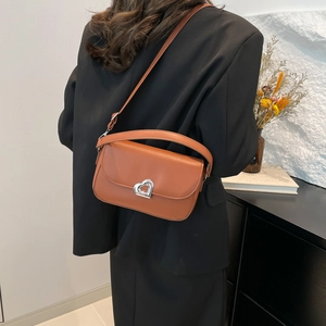 Caramel leather crossbody bag with silver heart buckle shown on model in black suit