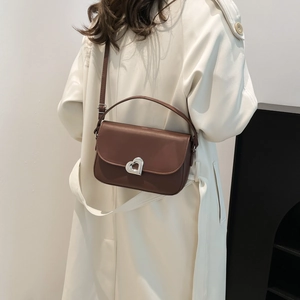 Brown leather saddle shoulder bag with silver heart buckle worn over a beige trench coat