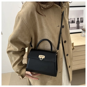 Detail einer schicken schwarzen quadratischen Handtasche mit goldener Schließe und Gurt