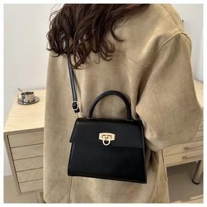 Detailansicht der schwarzen Handtasche mit Goldverschluss und Lederriemen von der Seite