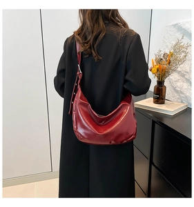 Detail of burgundy glossy leather hobo bag worn over the shoulder by a model