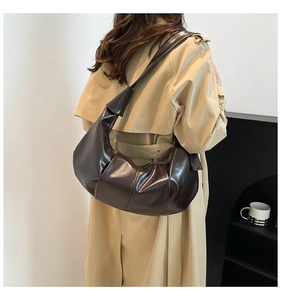 Macro shot of dark brown glossy leather hobo bag with pleated texture on a trench coat