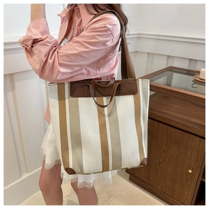 Detail of striped canvas tote showing brown leather reinforcement and durable handles