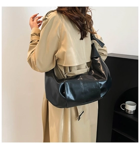 Glossy black pleated dumpling bag shown on shoulder with minimalist style on a model