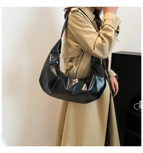 Detail view of a black glossy pleated crescent shoulder bag styled with a beige trench coat